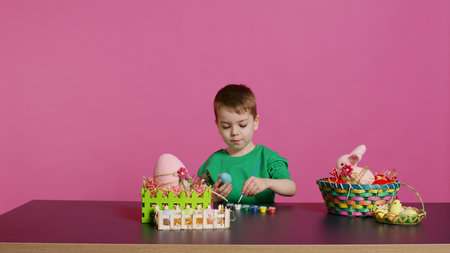 Joyful small kid painting eggs for easter holiday festivity in studio, using watercolor and art supplies. Smiling preschooler coloring festive ornaments in preparation for sunday. Camera B.の写真素材