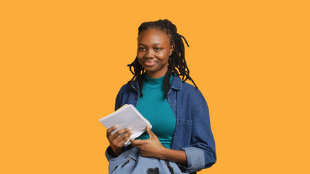 Joyous african american woman rummaging through backpack, looking for school notebooks, isolated over studio background. Merry teenager taking out university supplies out of rucksack, camera Aの写真素材