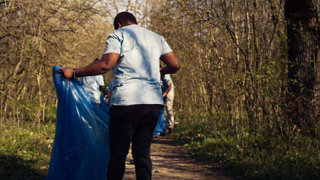 Diverse activists group using claw tools to grab trash and plastic, storing it in garbage disposal bags. People gathering to collect rubbish and recycling for sustainable lifestyle. Camera B.の写真素材