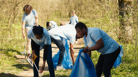 Environmental activists collecting rubbish and plastic waste in garbage bag, using littler cleanup tools to pick up trash from the forest. Women doing voluntary work to protect ecosystem. Camera A.の写真素材