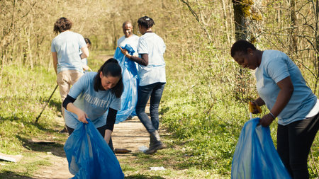 Group of diverse volunteers collecting rubbish from the woods and recycling in a garbage disposal bag, litter cleanup responsibility. Ecology activists picking up trash and plastic waste. Camera A.の写真素材