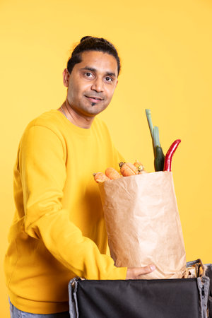 Portrait of cheerful deliveryman taking takeaway order out of bag, providing it to client. Joyous...