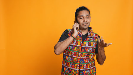 Man discussing with best friend over telephone call, enjoying leisure time. Upbeat person wearing indian attire talking with mate in phone call, isolated over studio backdrop, camera Bの写真素材
