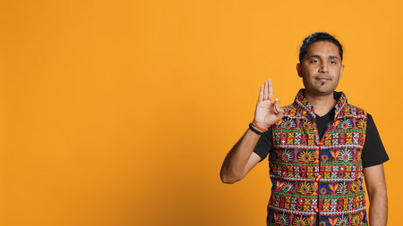 Indian man doing ok hand sign, feeling pleased, agreeing with satisfactory conclusion. Optimistic person doing okay symbol gesturing, offering positive feedback, studio background, camera Aの写真素材