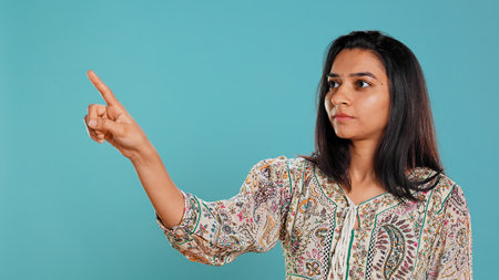 Salesman pointing around with finger, doing recommendation, talking with audience. Indian woman showing copy text space, doing advertisement, isolated over studio background, camera Bの写真素材