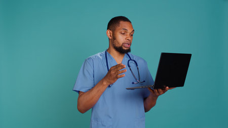 Friendly upbeat medic doctor in videocall meeting using laptop, providing treatment plan. Jolly hospital staff member listening to patient health problems in online telemedicine call, camera Bの写真素材