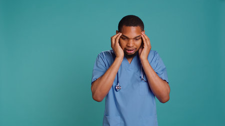 Fatigued nurse suffering from migraine pain after tiresome day at work. Hospital worker isolated over studio background affected by distressing headache during demanding job shift, camera Bの写真素材