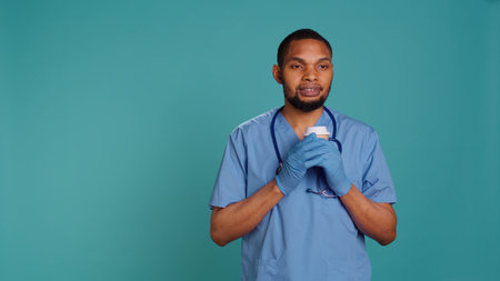 Happy male nurse enjoying fresh cup of coffee during job shift break. Cheerful healthcare specialist isolated over studio background drinking hot beverage while at work, camera Bの写真素材