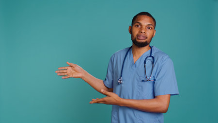 Portrait of african american nurse pointing hands towards empty space, doing advertising, talking with audience. Healthcare employee doing promotional ad, showing copy text, studio backdrop, camera Bの写真素材