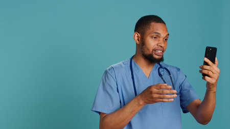 Male nurse in videocall meeting using mobile phone, greeting people. Healthcare expert in online telemedicine call with patients using smartphone, isolated over studio background, camera Aの写真素材