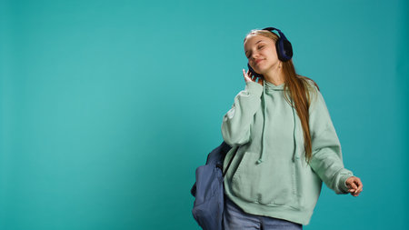 Happy girl wearing headphones having fun, dancing on rhythm, enjoying leisure time. Cheerful woman entertaining herself doing funky movements on music, studio background, camera Bの写真素材