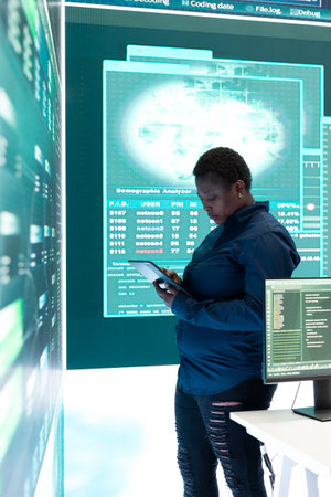 Governmental hacker woman working with a tablet and big screen in high tech office, focusing on data security and cyber operations. Cybercrime, server protection and threat detection.の写真素材