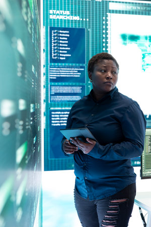 Woman IT specialist working on a tablet in a monitoring room with big screens and advanced technology.の写真素材