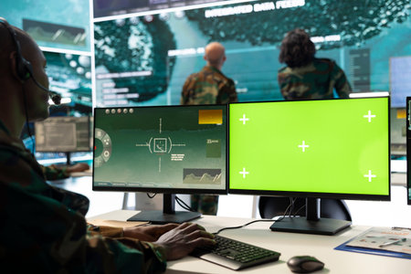 Serviceman operates on surveillance footage and green screen display, monitoring battlefield...