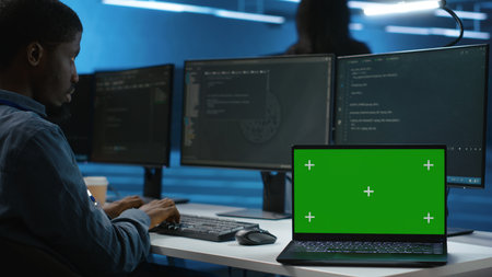 Isolated screen laptop next to programmer coding in server farm, ensuring valuable data remains...