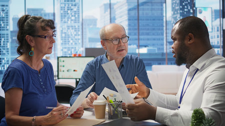 Senior people discussing a pension financial strategy with broker, receiving advice from agency expert to secure future income and family expenses. Guaranteeing life insurance plans. Camera B.の写真素材