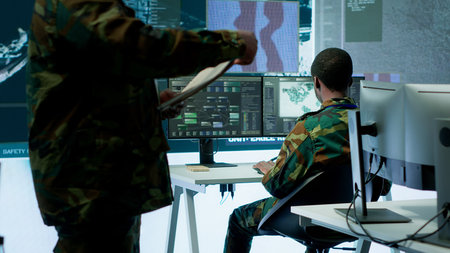 Skilled team of military specialists operate advanced technology and a big screen in a control...