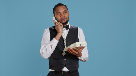 Bellboy concierge staff answering landline phone call to make reservations, discussing with clients...