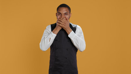Restaurant staff covering his eyes, mouth and ears against evil in studio, presenting three wise monkeys metaphor. Waiter doesnt see, hear or speak as a concept, hospitality industry. Camera B.の写真素材
