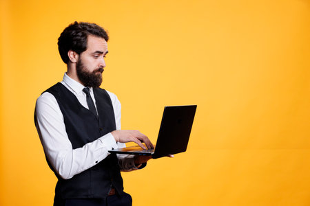 Restaurant worker checking website on laptop, browses online in studio to create new price list on restaurant menu. Young adult uses pc to navigate through social media app on camera.の写真素材