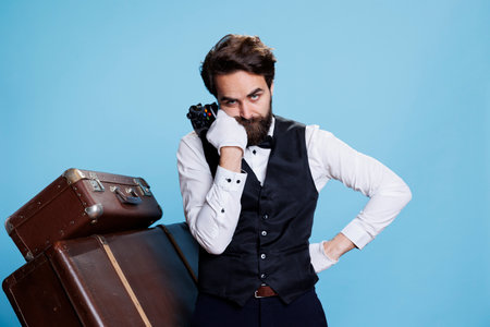 Hotel concierge losing video gameplay, being unsatisfied and negative in studio. Bellhop in suit against blue background with joystick while he feels disappointed about lost online competition.の写真素材