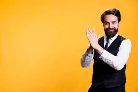 Positive employee clapping hands on camera, feeling happy after finding out about success. Young man with butler occupation applauding and giving confidence boost to person, cheering.の写真素材