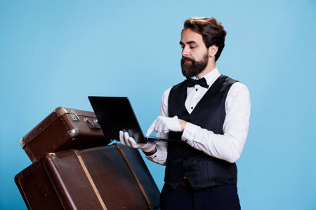 Hotel concierge with laptop in hand symbolizing role as porter or doorkeeper, leveraging modern technology to provide assistance. Bellhop checking online bookings or reservations on pc.の写真素材