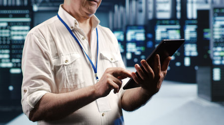 Tech savvy professional navigating network of server rigs in industrial cloud computing company. Manager with tablet doing assessments and optimizations in data center, preventing system pitfallsの写真素材