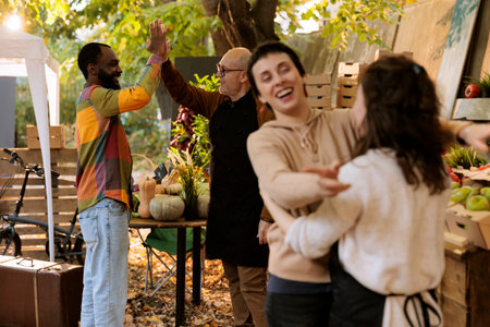 Thankful elderly man gives regular customer a high five while offering fresh organic fruits and vegetables at farmers marketplace. At greenmarket, local vendors greet customers with enthusiastic grin.の写真素材
