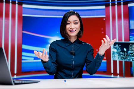 Asian journalist on daily reportage in studio, talking about latest global incidents on live broadcast transmission. Woman presenter creating television content by reading headlines.の写真素材