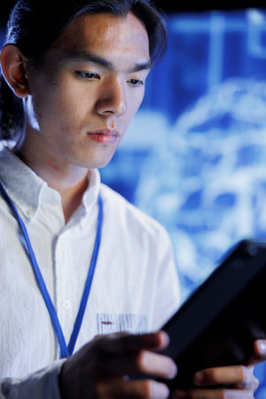 Computer scientist using tablet in data center to maintenance artificial intelligence neural networks simulating human thought processes in computerized model. Asian man doing checkup on AI systemsの写真素材