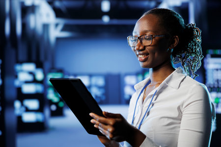 Smiling woman between server hub rows providing processing resources for businesses worldwide. Happy admin fixing data center mainframes tasked with managing massive databasesの写真素材