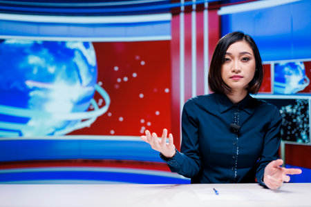 Asian host reporting live news on television broadcast, talking about daily events in newsroom. Woman journalist giving insight on latest topics, creating media television content.の写真素材
