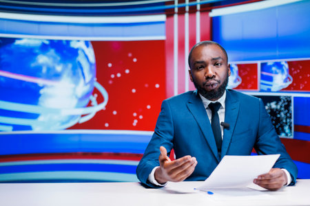 Anchorman reading news headlines from papers, presenting exclusive details about latest events worldwide. African american newscaster broadcasting politics or economics information, tv network.の写真素材