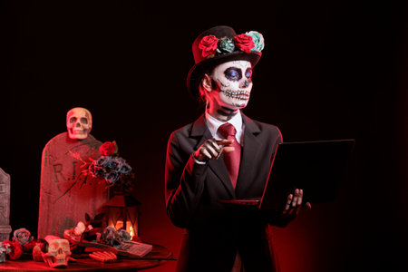 Portrait of woman wearing flower crown types on notebook in graveyard, celebrating Day of the Dead. Mysterious lady in formal suit working on laptop, surrounded by funeral items during Halloween eventの写真素材