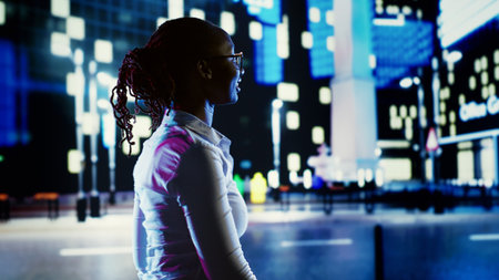 Euphoric person dancing around and greeting other people, walking on town boulevard during nighttime. Exultant woman enjoying herself while strolling on metropolitan avenues surrounded by skyscrapersの写真素材