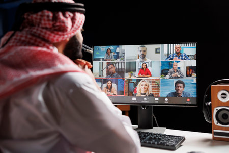 Selective focus on computer screen displaying video call between Muslim businessman and his colleagues. Detailed image of Arab guy video conferencing his team, having online communication.の写真素材