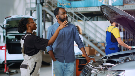 Mechanic in auto repair shop using augmented reality hologram to visualize car components to client. Expert using AR holographic technology to show customer vehicle repairments to be doneの写真素材