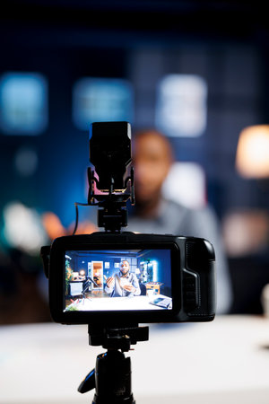 Focus on professional video production camera used for capturing footage of tech enthusiast in blurry background filming smart light bulb review for online audience, showcasing home automation systemの写真素材
