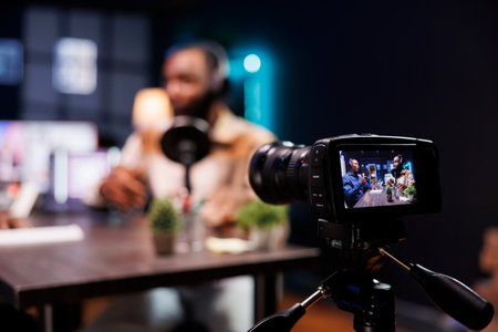 Detailed view of professional camera filming a live talk show between two black men in home studio....