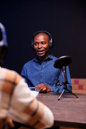 Black male guest speaking into microphone, answering questions from radio program host. African american man being interviewed using audio equipment to record an online talk show at home.の写真素材