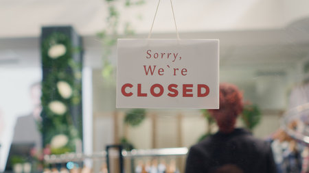 Worker closing down store in order to do restocking in elegant high end fashion boutique. Employee adding closed sign on clothing store door to be able to add stylish garments from new collectionの写真素材