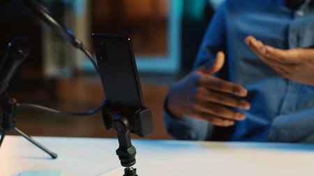 Close up shot of smartphone on holder used by online star in dimly lit home studio to film video for online streaming platforms. Mobile phone being used by influencer to record footage, panning shotの写真素材