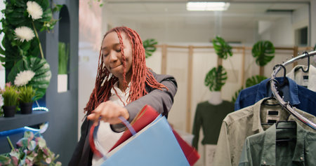 Tracking shot of customer dancing in clothing store during promotional season after finding cheap garments. Woman excited about sales in fashion boutique, leaving with shopping bags full of clothesの写真素材