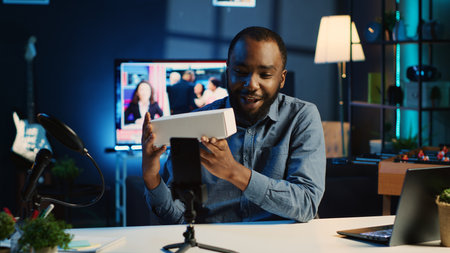 Tech content creator filming packaged product unboxing in neon lights personal home studio using professional equipment. Influencer showing sponsoring partner merchandise, urging subscribers to buy itの写真素材