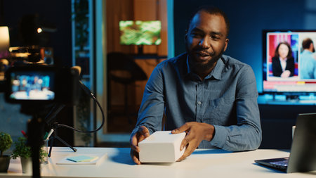 BIPOC tech content creator filming product unboxing of newly released smartphone, urging audience to purchase it too. Internet star payed by sponsor to show phone to subscribersの写真素材
