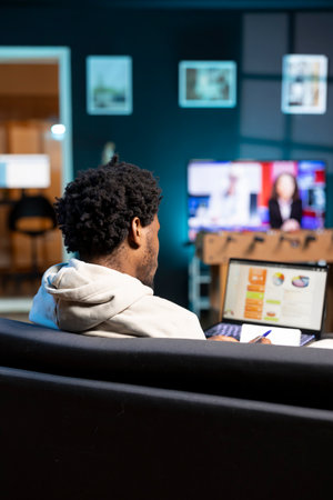 BIPOC person working in personal office, checking statistical data financial graphs on laptop screen. Freelancer in apartment living room comparing business graphic economic numbersの写真素材