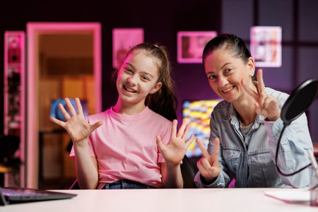 Daughter and mother filming content for online streaming family channel in pink neon studio. Woman doing parenting vlog, excited about her kid receiving high grades at schoolの写真素材