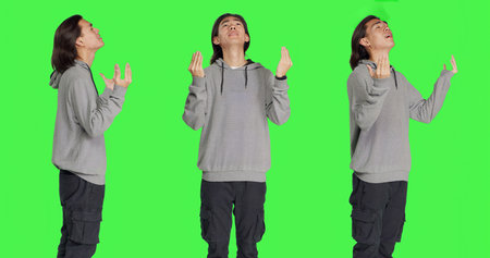 Model with belief praying to God against greenscreen studio backdrop, hoping for fortune and good things. Young religious man acting spiritual with prayer, feeling hopeful.の写真素材
