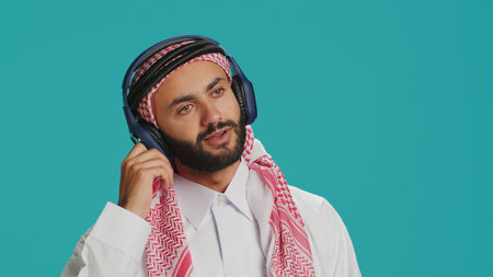 Groovy man dancing on camera, listening to modern tunes on headset and having fun in studio. Middle eastern man in traditional attire showing funky dance moves and singing songs.の写真素材